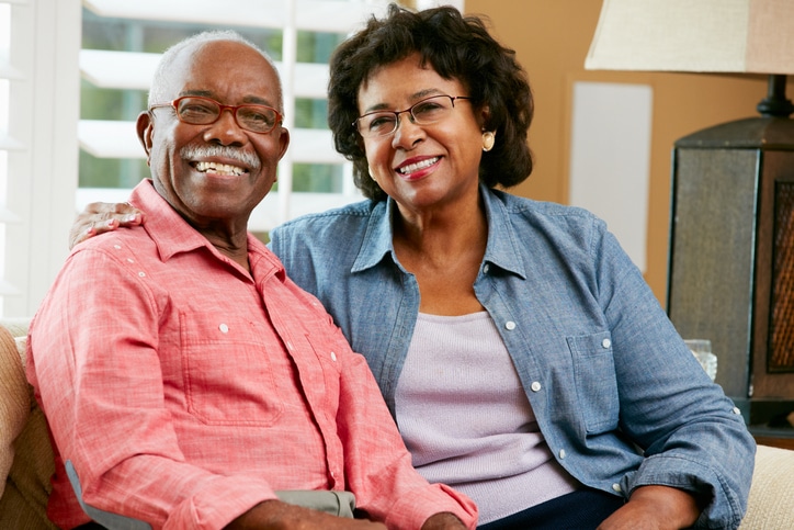 Portrait Of Happy Senior Couple At Home Sitting On Sofa Smiling To Camera